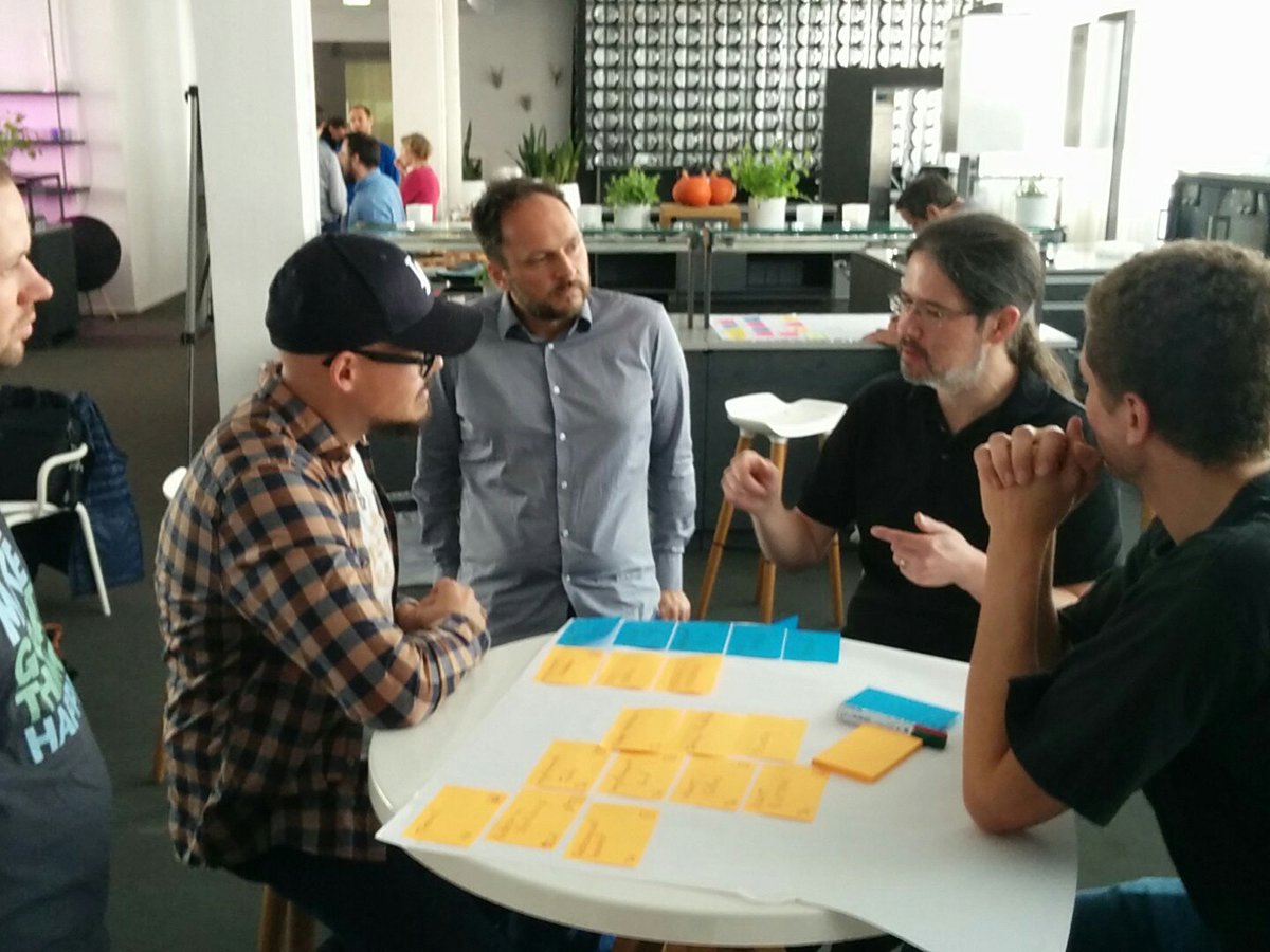 J. B. working with a client at a workshop, standing at a table with three employees, mapping a value stream
